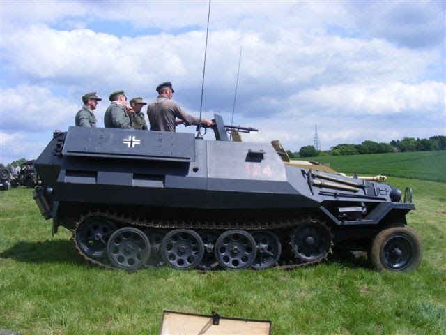 Members in uniform aboard a grey half-track at an event