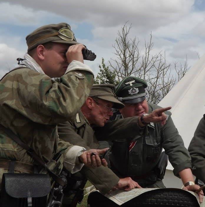 Three men in Wehrmacht uniform, one with binoculars, studying a map