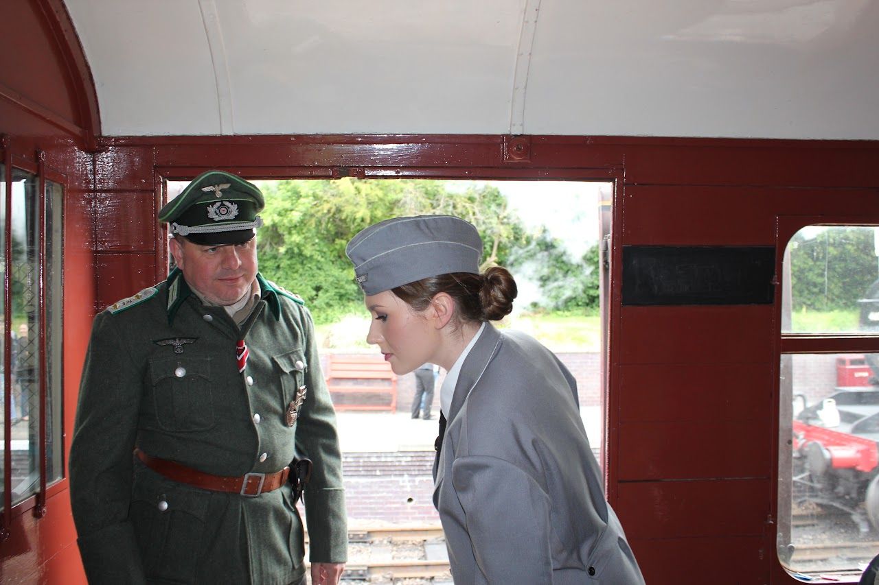 A Helferin in a grey uniform and side cap beside an officer in a railway carriage