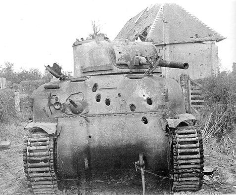A knocked-out M4A1 Sherman tank beside a damaged building