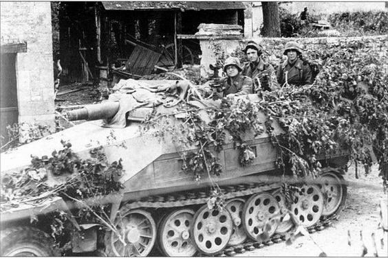 Soldiers aboard a camouflaged Sd.Kfz. 251/9 half-track with a short 75 mm gun