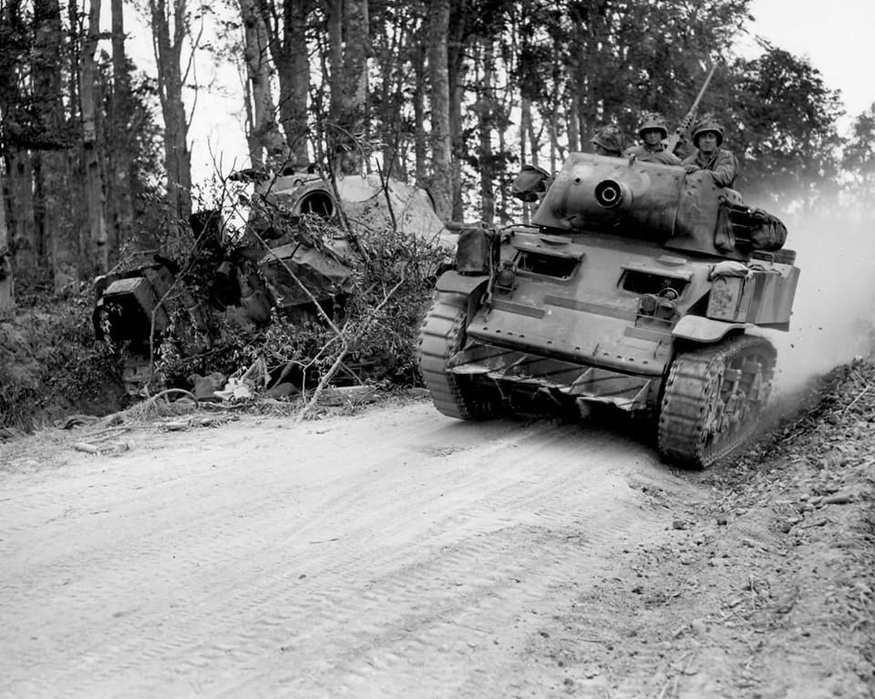 An American M8 armoured car passing a wrecked Panther on a forest road