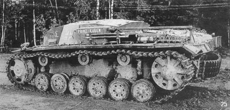 A StuG III assault gun in a wood, its side skirts caked in mud
