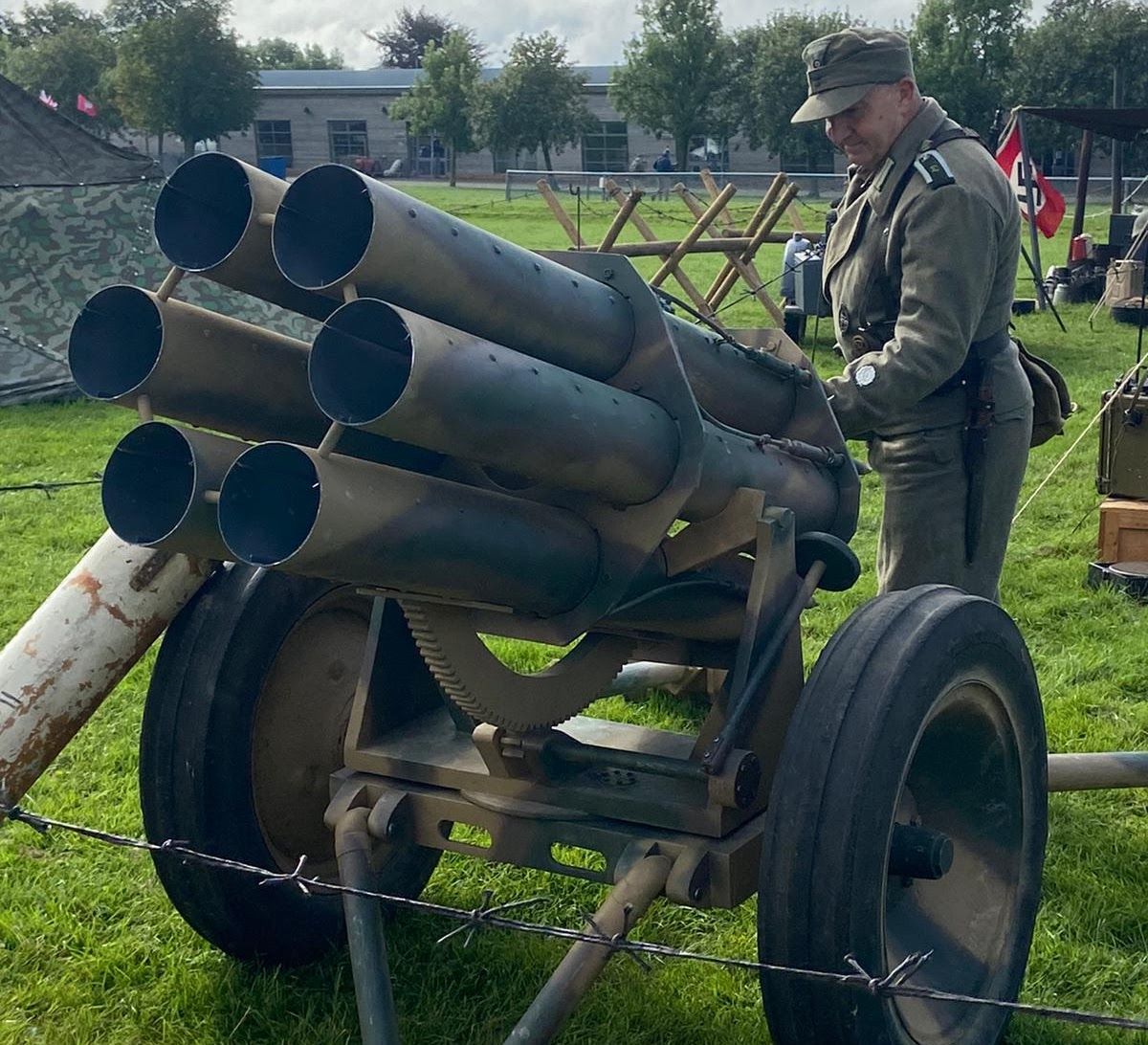 A member in uniform standing beside a six-barrelled Nebelwerfer rocket projector on grass