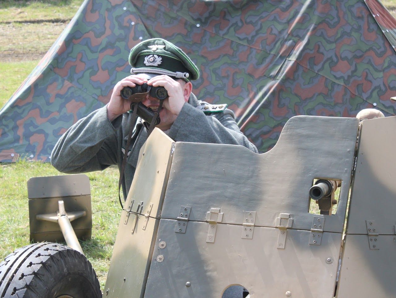 A member in uniform looking through binoculars over the shield of a PaK 36 gun