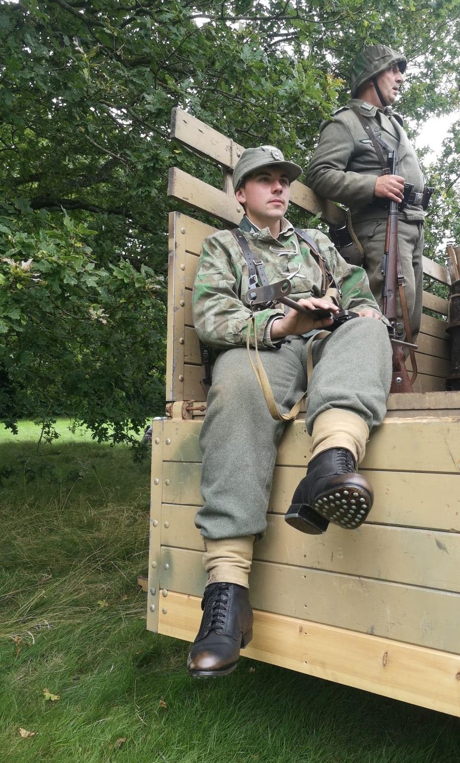 A soldier in field uniform sitting on the tailboard of a wooden truck